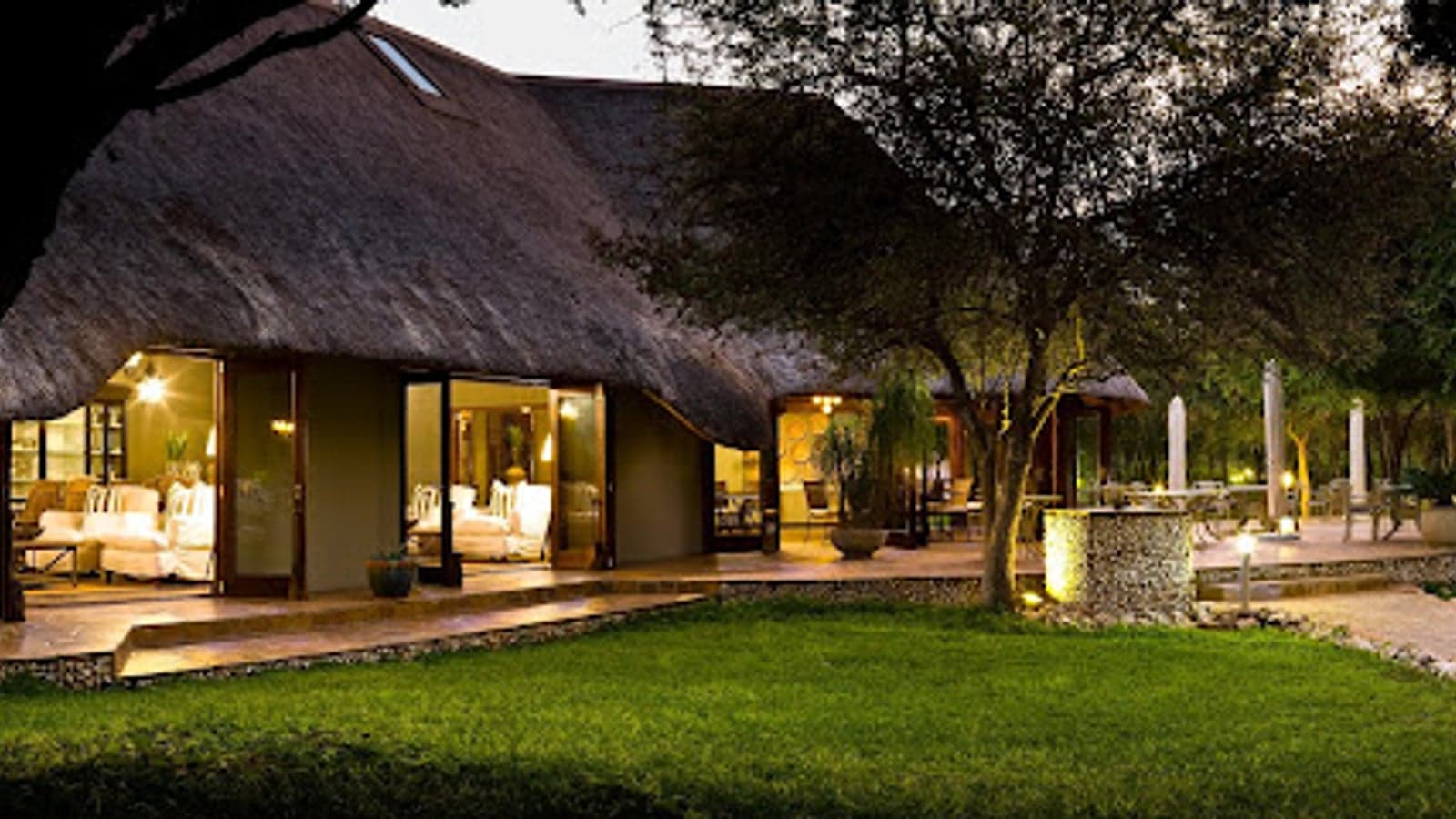 Thatched lounge and terrace at Mushara Lodge, Etosha, lit at dusk