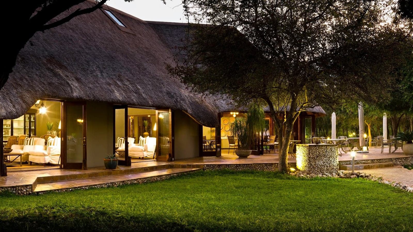 Thatched lounge and terrace at Mushara Lodge, Etosha, lit at dusk