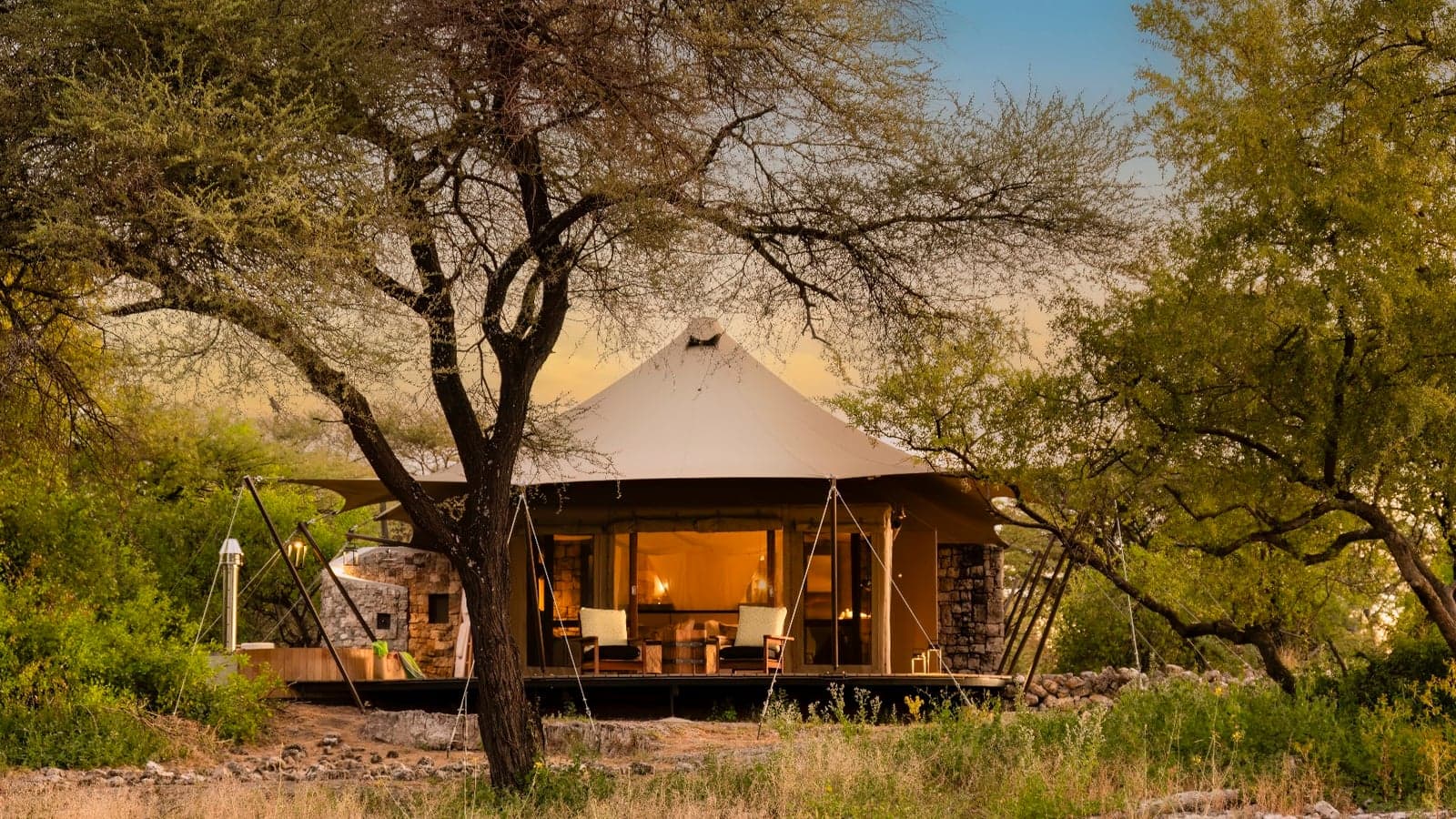 A tented suite at dusk under a large tree at Onguma Tented Camp, Etosha